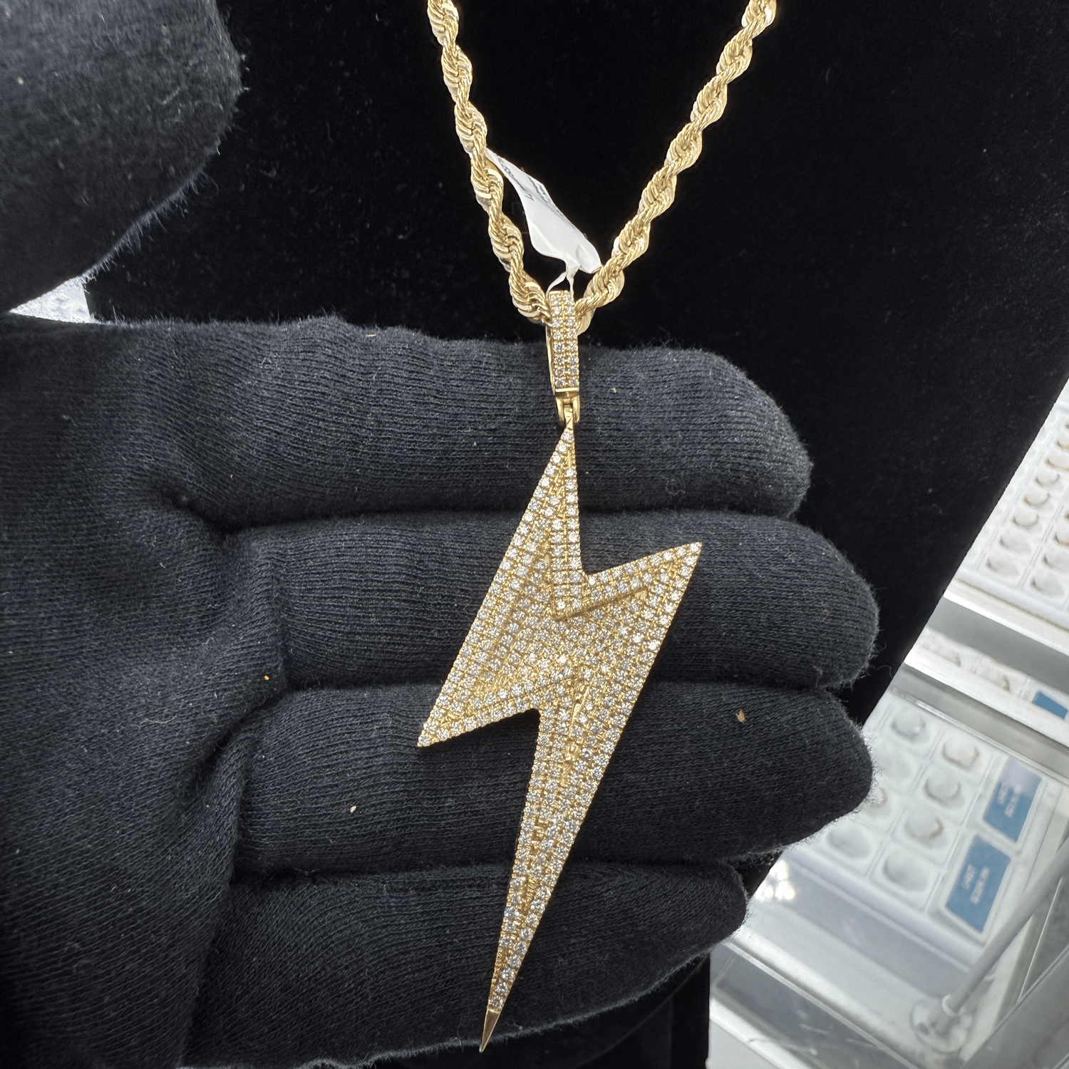 Gold lightning bolt pendant held in a black gloved hand against a blurred background