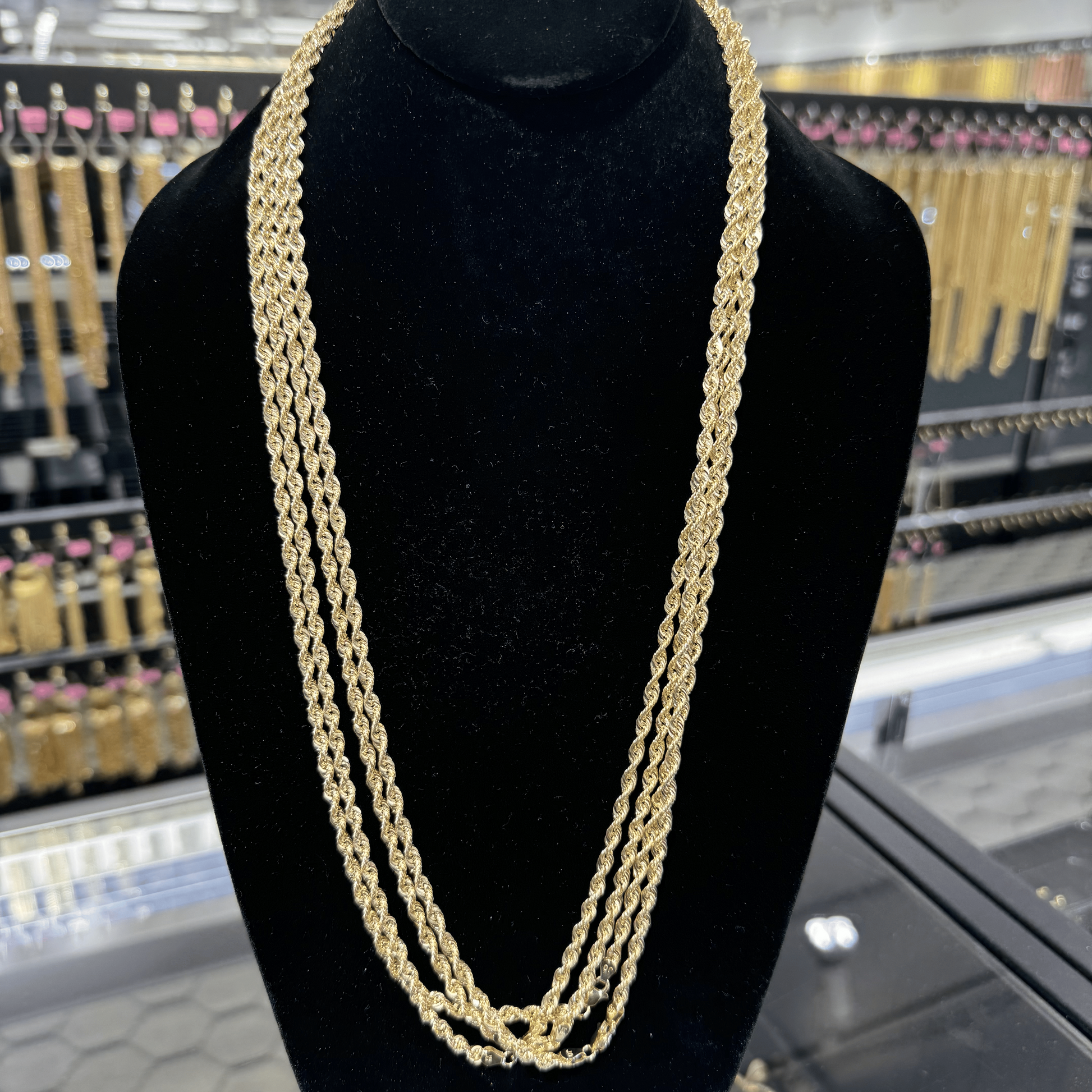 Gold chain necklace on a black mannequin bust in a store setting.